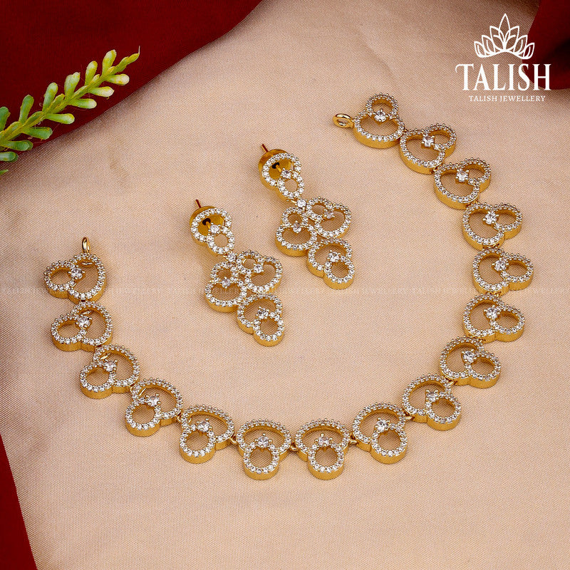 A gold and diamond jewelry set featuring a necklace and matching earrings with circular designs, displayed on a fabric background with a small green leaf accent. The brand name "Talish Jewellery" is visible in the top right corner.