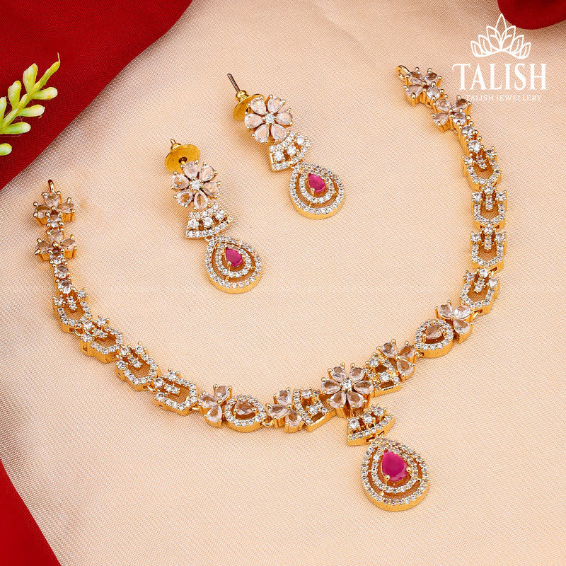 A gold necklace and earring set with intricate designs, featuring pink gemstones and white stones, displayed on a red and beige background.