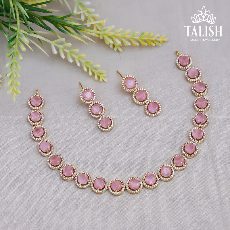 A jewelry set featuring a necklace and earrings with pink gemstones surrounded by small white stones, displayed on a light background with decorative green foliage.