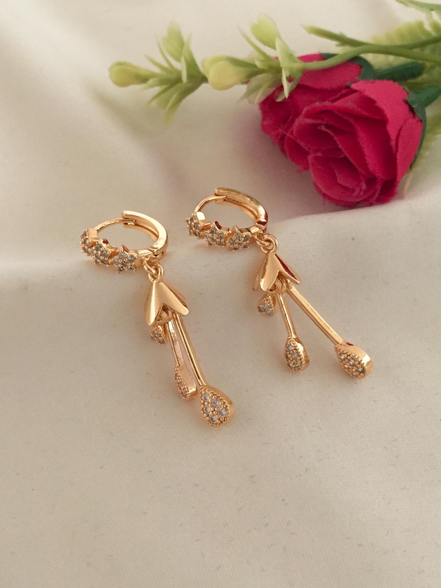 Gold hoop earrings with dangling arrow and teardrop-shaped charms, adorned with small crystals.