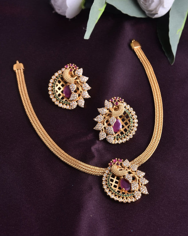 A gold necklace and matching earrings set with intricate designs, featuring purple gemstones and white crystals, displayed on a dark fabric background.