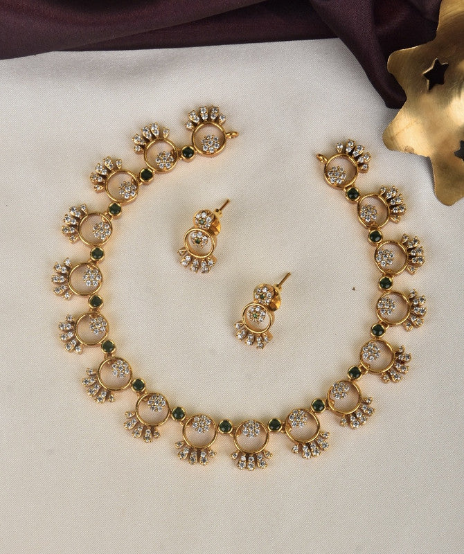 A gold necklace and matching earrings set with circular designs, adorned with white and green stones.