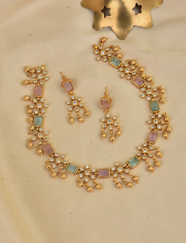 A gold necklace and matching earrings set with square pastel-colored stones and intricate detailing.