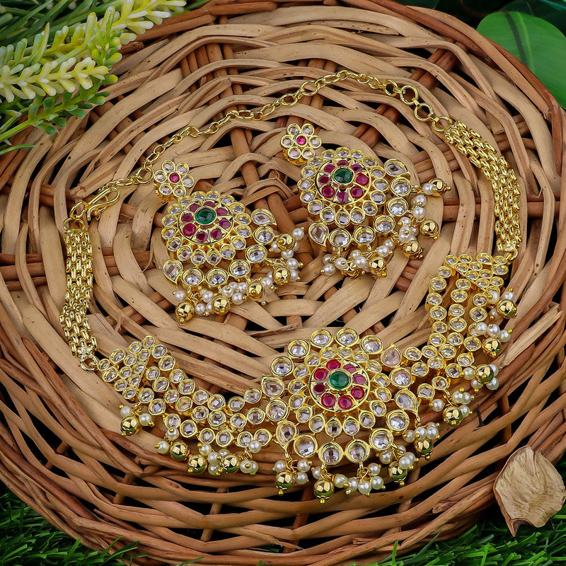 A set of traditional gold jewelry with intricate designs, featuring a necklace and matching earrings adorned with red, green, and clear stones, displayed on a woven basket.