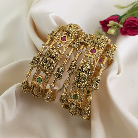 Two intricately designed gold bangles adorned with small statues, colorful gemstones, and white stones.