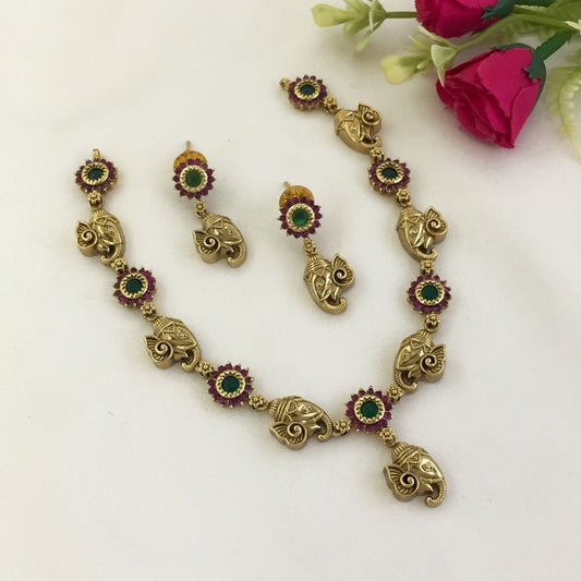 A gold necklace and earring set with elephant-shaped pendants and green and red gemstone accents.