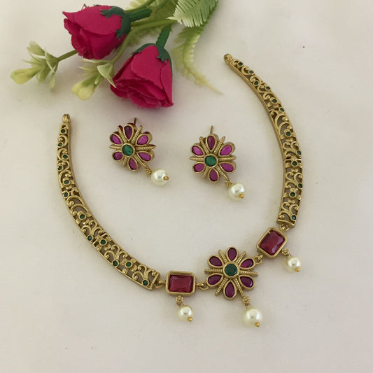 A set of traditional jewelry consisting of a necklace and matching earrings. The necklace features intricate gold detailing with red and green gemstones and pearl accents. The earrings are designed to match with similar gemstones and pearl drops.