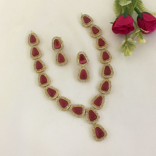 A jewelry set consisting of a necklace and a pair of earrings, featuring red teardrop-shaped stones surrounded by small clear stones.