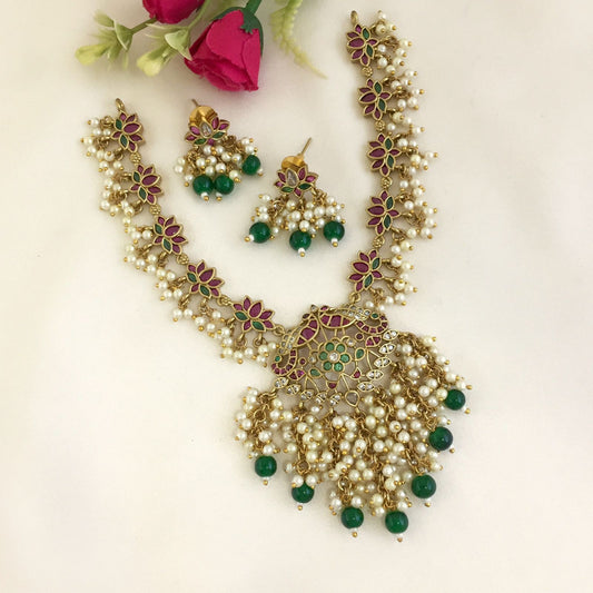 A set of traditional jewelry consisting of a necklace and matching earrings. The necklace features intricate floral designs with pearls and green beads, while the earrings have a similar design with dangling pearls and green beads.