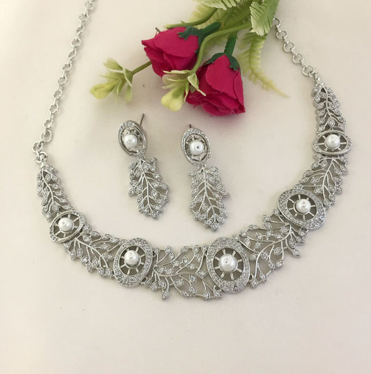 A silver necklace and matching earrings set with intricate leaf designs and embedded pearls.