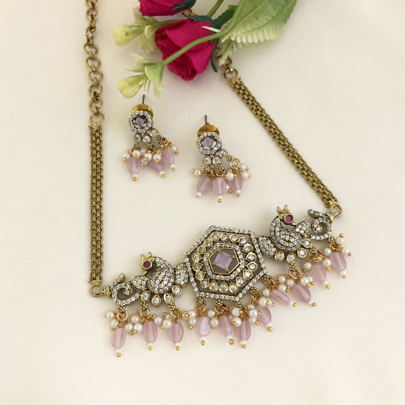 A gold necklace with intricate designs, featuring a central hexagonal pendant adorned with pink and white stones, and matching earrings.