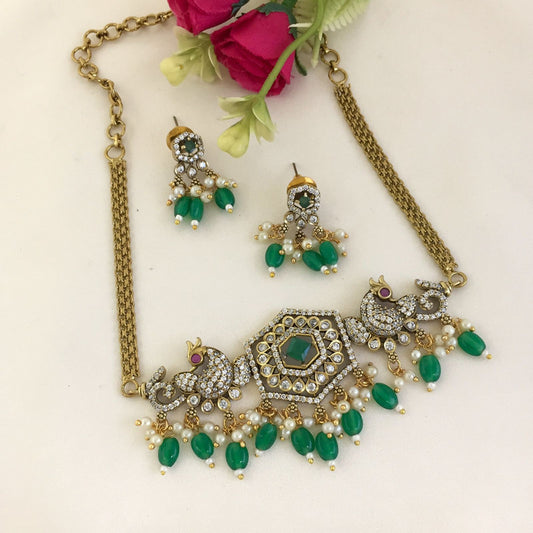 A gold necklace with intricate designs featuring peacock motifs, green gemstones, and pearl accents, accompanied by matching earrings.