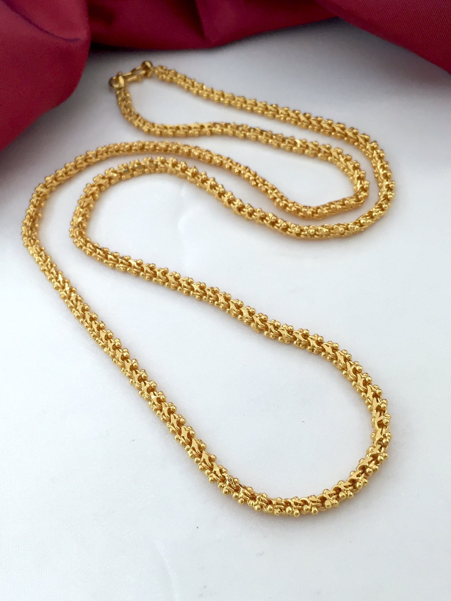 A gold chain necklace with an intricate, textured design displayed on a white surface.