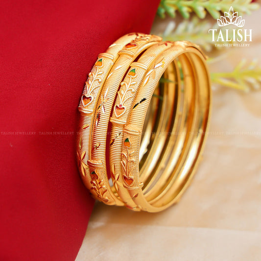 A set of intricately designed gold bangles with red and green enamel accents, displayed on a red fabric background.