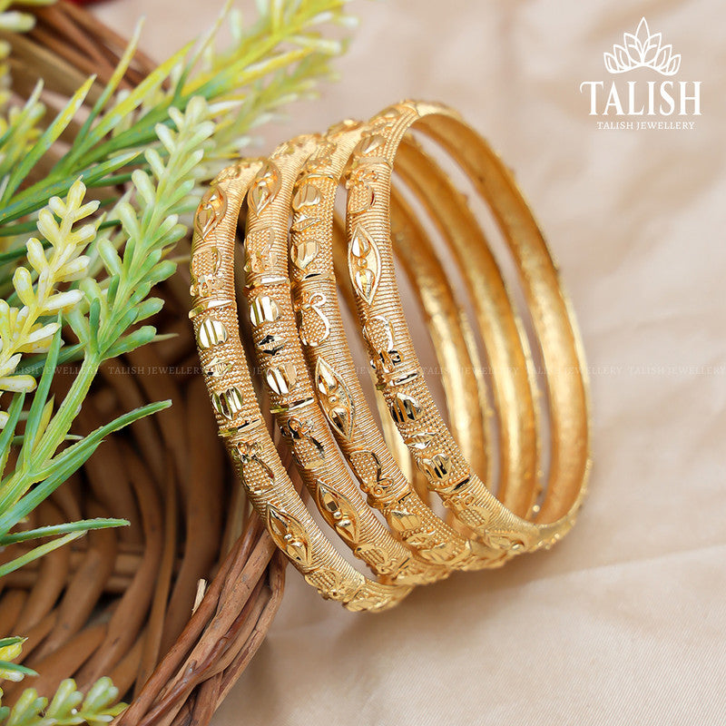 A set of intricately designed gold bangles displayed in a woven basket with green foliage nearby.