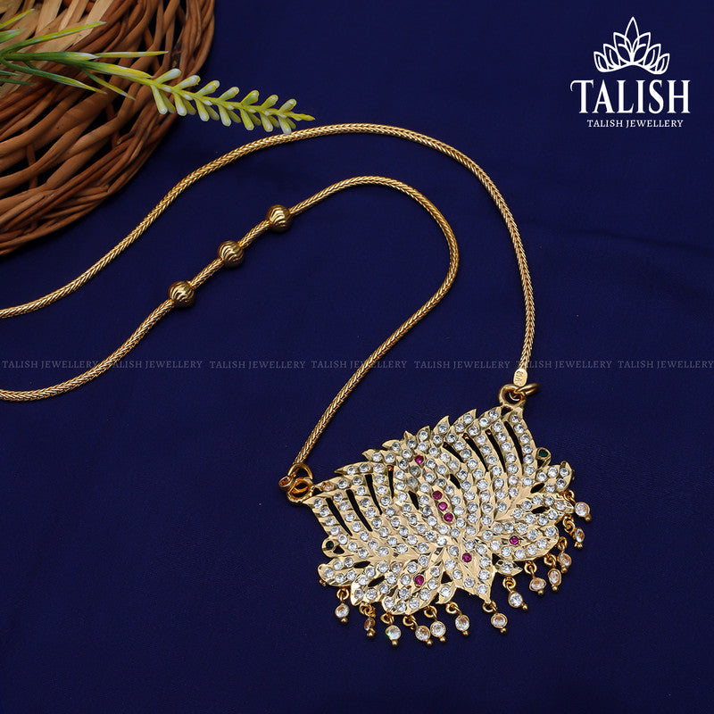 A gold necklace with an intricate pendant design featuring white and red stones, displayed on a dark blue fabric background. A wicker basket is partially visible in the corner.