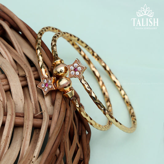 A pair of intricately designed gold bangles with star-shaped embellishments, featuring small colorful gemstones, placed on a woven basket.