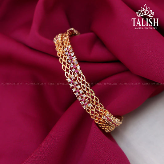 A gold bracelet with intricate designs and embedded pink gemstones, displayed on a rich magenta fabric.