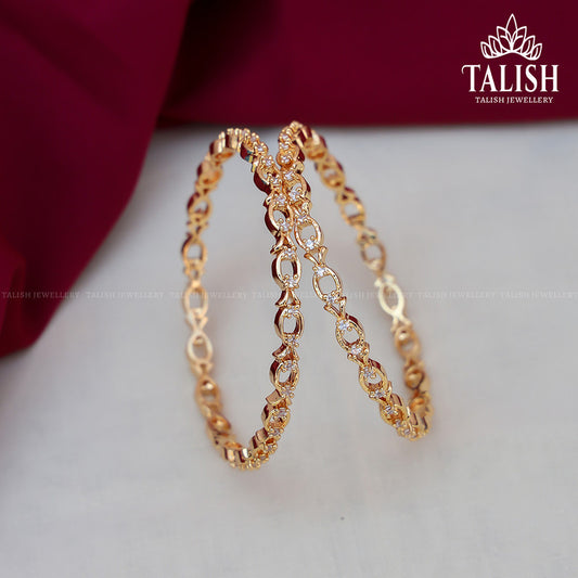 A pair of intricately designed gold bangles on a red fabric background, with the Talish Jewellery logo in the corner.