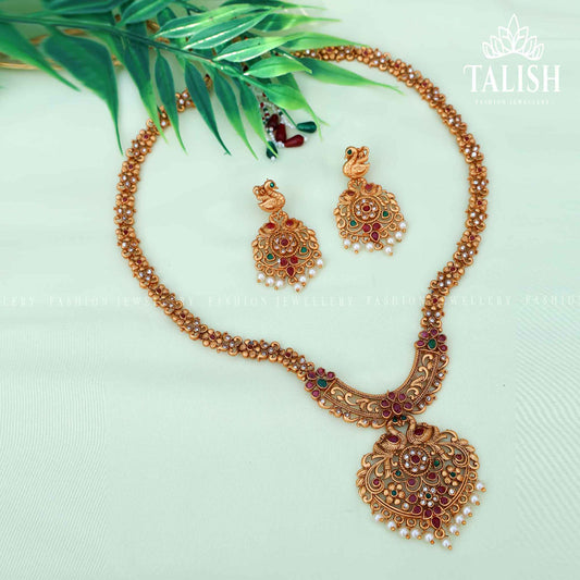 Elegant antique gold-plated necklace set featuring intricate designs, accompanied by matching earrings, displayed on a soft fabric background.