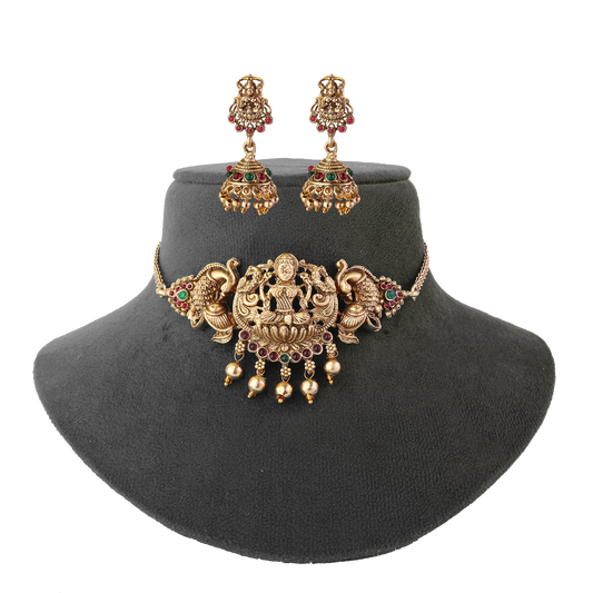 Gold necklace and earrings set with intricate designs and colorful gemstones displayed on a black stand.