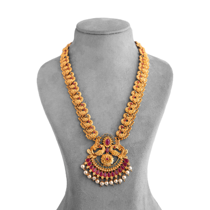 Gold necklace with intricate design, featuring red gemstones and pearl accents, displayed on a grey mannequin bust.