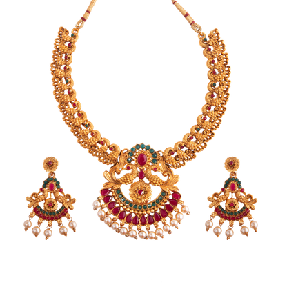 A gold necklace set with intricate designs, featuring red and green gemstones, and matching earrings adorned with pearl drops.