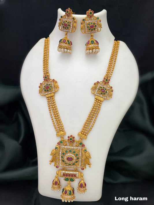 A long gold necklace with intricate designs, featuring square-shaped pendants adorned with red, green, and white stones, accompanied by matching earrings.