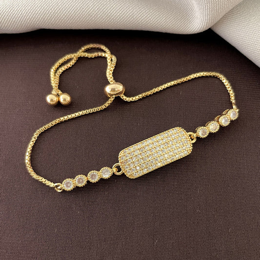 A gold bracelet with a rectangular, diamond-encrusted centerpiece and circular diamond accents on a dark surface.