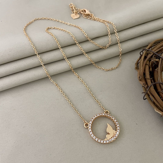 A gold necklace with a circular pendant featuring a butterfly design in the center, surrounded by small gemstones.