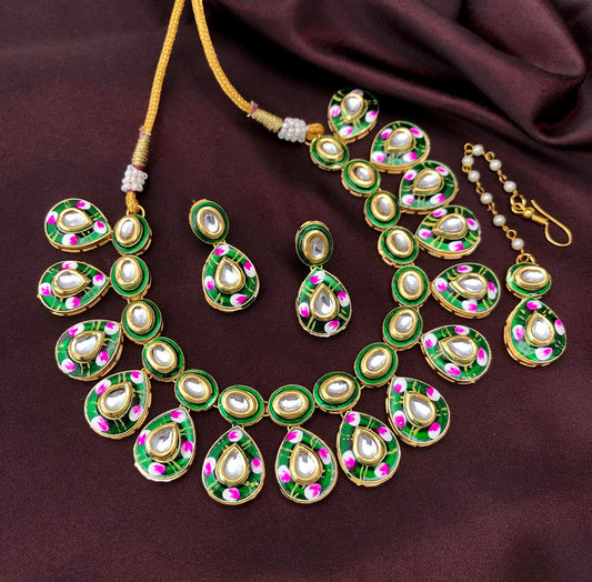 A traditional jewelry set featuring a necklace, earrings, and a maang tikka. The pieces are adorned with green and pink enamel work, gold detailing, and white stones. The necklace has a series of teardrop-shaped pendants, and the earrings and maang tikka match the design.