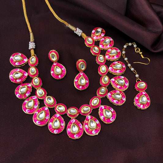 A set of traditional jewelry featuring a necklace, a pair of earrings, and a maang tikka, all adorned with pink and white enamel work and pearl-like stones.