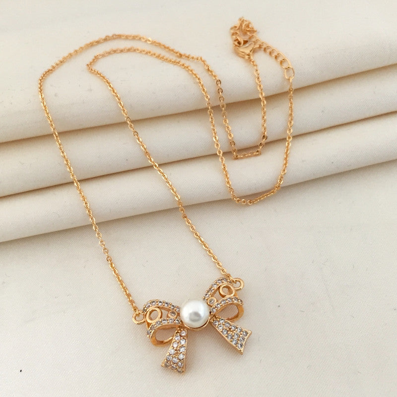 Gold necklace with a bow-shaped pendant adorned with rhinestones and a central pearl.