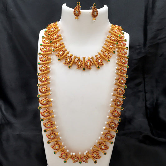 A set of traditional gold jewelry featuring a long necklace with intricate designs, adorned with red and green gemstones and small white pearls, accompanied by matching earrings.