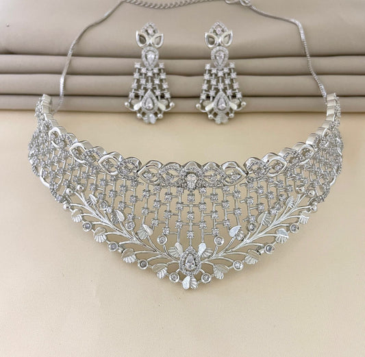 A set of intricate silver jewelry consisting of a choker necklace and matching earrings, adorned with numerous small, sparkling stones arranged in elaborate patterns.