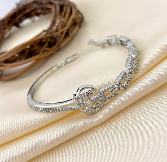 A silver bracelet with intricate square and circular designs, featuring small embedded stones.