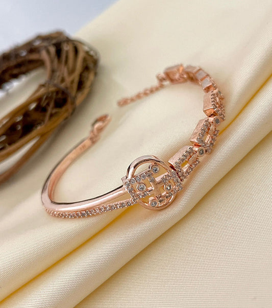 A rose gold bracelet with intricate designs and embedded gemstones, displayed on a light fabric.