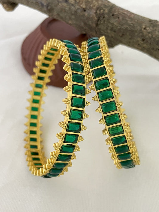 Two gold bangles with green square gemstones.