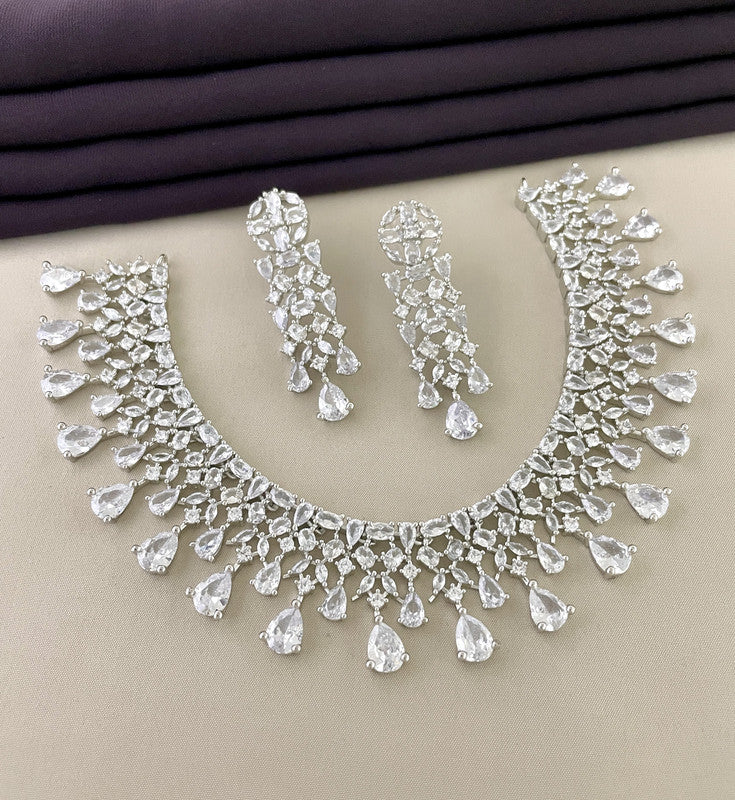 A silver necklace and matching earrings set with intricate design and teardrop-shaped crystals.
