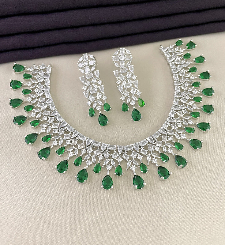 A silver necklace and matching earrings set adorned with green teardrop-shaped gemstones and clear crystals.