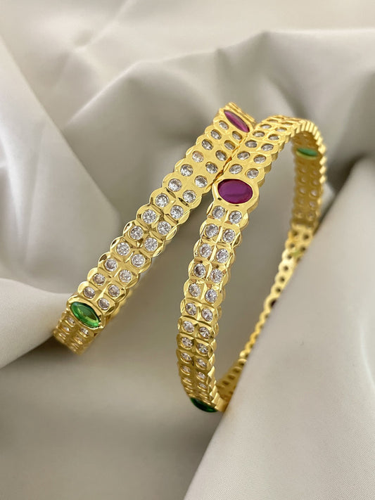 Two gold bangles adorned with diamonds and colorful gemstones.