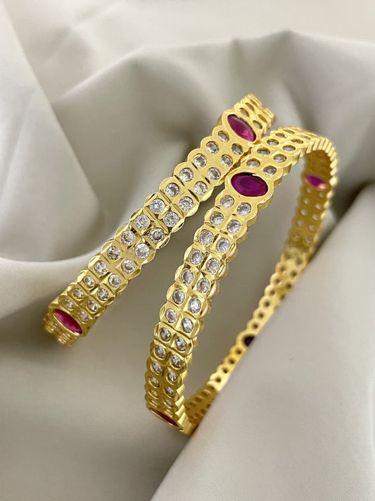 Two gold bangles adorned with clear and pink gemstones.