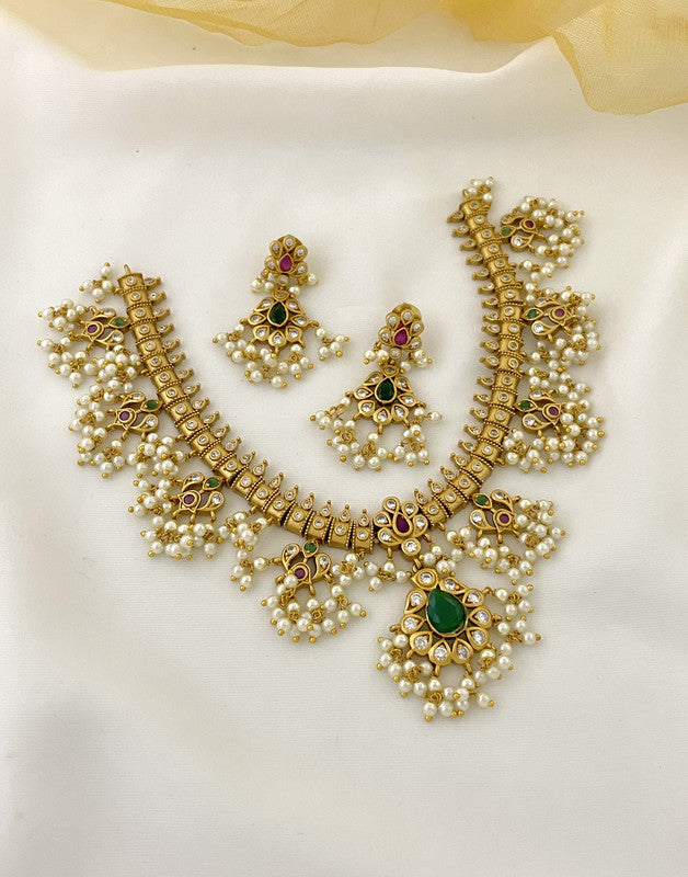 A gold necklace with intricate design and pearl embellishments, accompanied by matching earrings.