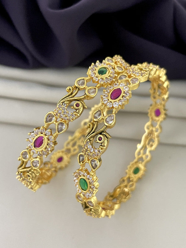 Two intricately designed gold bangles adorned with green, red, and white gemstones.