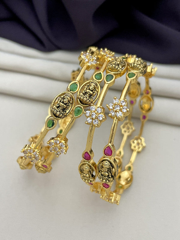 Gold bangles adorned with intricate designs, green and red gemstones, and white crystals.