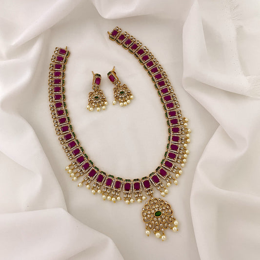 A gold necklace with red gemstones and pearl accents, accompanied by matching earrings.