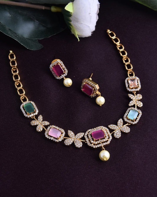 A gold necklace and earring set featuring rectangular gemstones in various colors, surrounded by small diamonds, and adorned with floral designs and pearl accents.