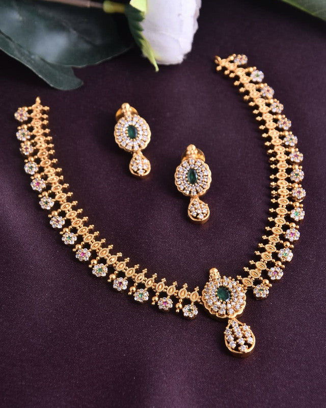 A gold necklace set with intricate designs, featuring green and white stones, accompanied by matching earrings.