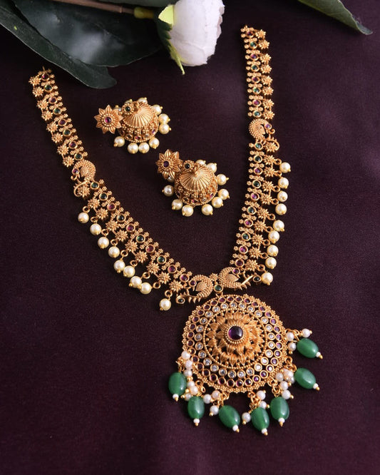 A traditional gold necklace set with intricate designs, featuring a large circular pendant adorned with green beads and matching earrings.