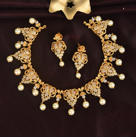 A gold necklace set with intricate designs, adorned with pearls and white stones, accompanied by matching earrings.